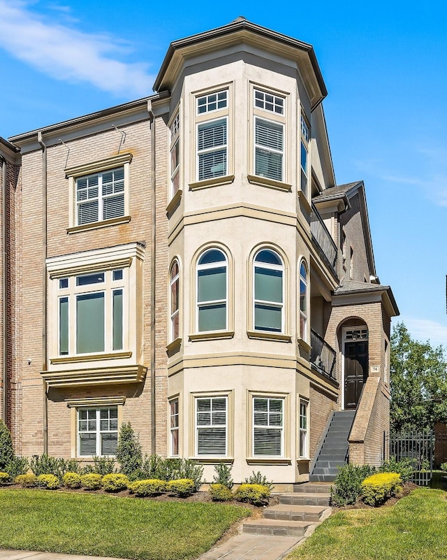 view of front of property featuring stairs, brick siding, and stucco siding