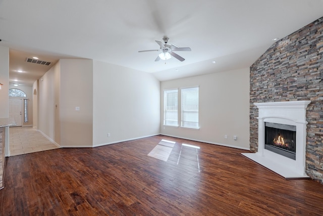 unfurnished living room featuring wood finished floors, visible vents, a warm lit fireplace, ceiling fan, and vaulted ceiling