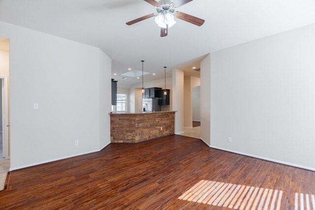 unfurnished living room with arched walkways, baseboards, ceiling fan, and dark wood-style flooring