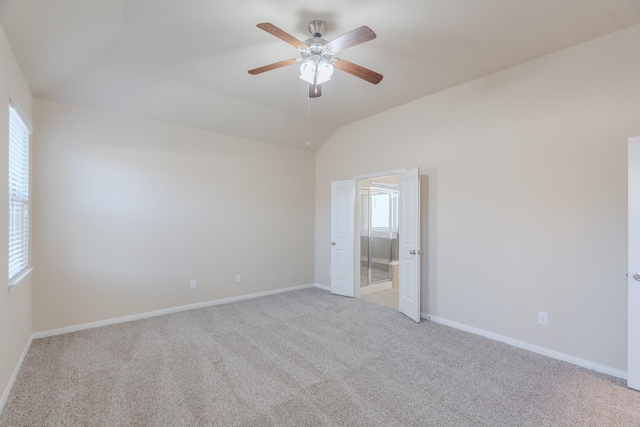 unfurnished bedroom with baseboards, light carpet, ensuite bathroom, and vaulted ceiling