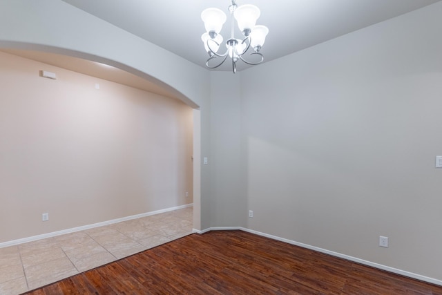 empty room with baseboards, arched walkways, a notable chandelier, and wood finished floors