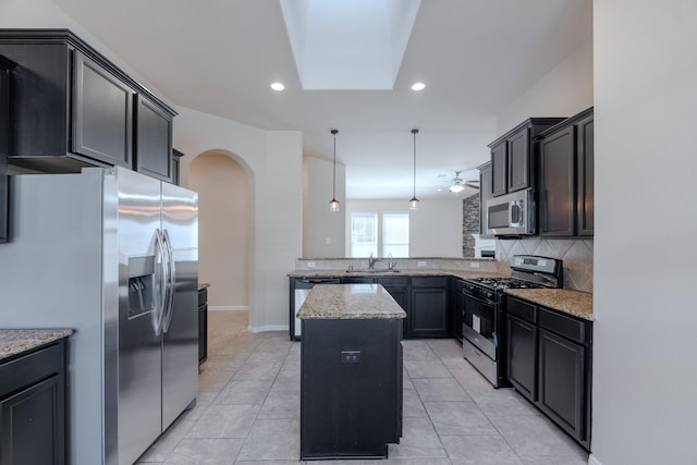 kitchen with a sink, tasteful backsplash, a center island, arched walkways, and appliances with stainless steel finishes