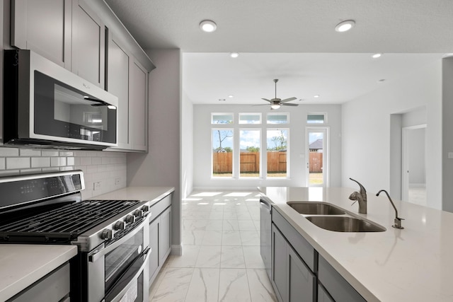 kitchen with backsplash, gray cabinetry, marble finish floor, stainless steel appliances, and a sink