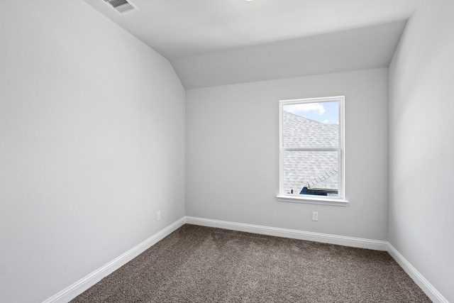 spare room featuring visible vents, baseboards, lofted ceiling, and dark carpet