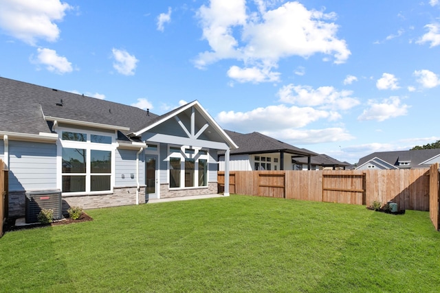 rear view of house featuring stone siding, central AC, fence, a yard, and roof with shingles