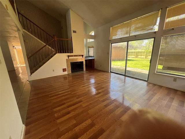 unfurnished living room featuring stairs, wood finished floors, a towering ceiling, and a tile fireplace