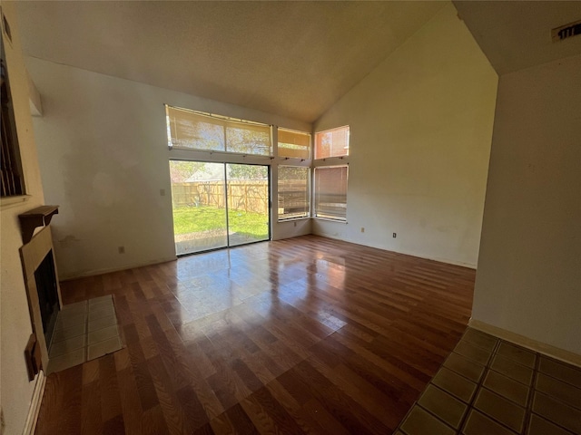 unfurnished living room with visible vents, high vaulted ceiling, a fireplace with flush hearth, and wood finished floors