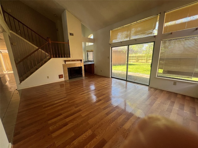 unfurnished living room with high vaulted ceiling, wood finished floors, baseboards, stairs, and a tile fireplace