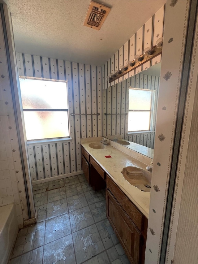 full bathroom with baseboards, visible vents, wallpapered walls, a sink, and a textured ceiling