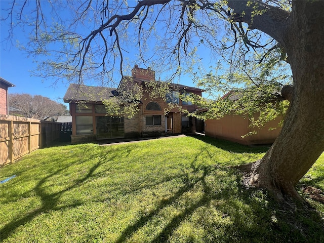 rear view of property with a lawn, a fenced backyard, and a chimney