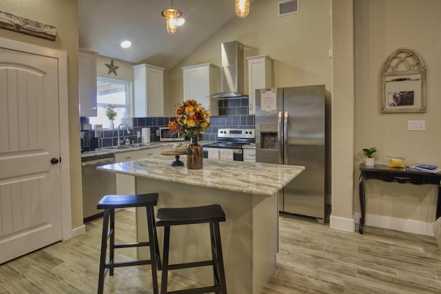 kitchen featuring visible vents, light wood-style flooring, a sink, stainless steel appliances, and wall chimney exhaust hood