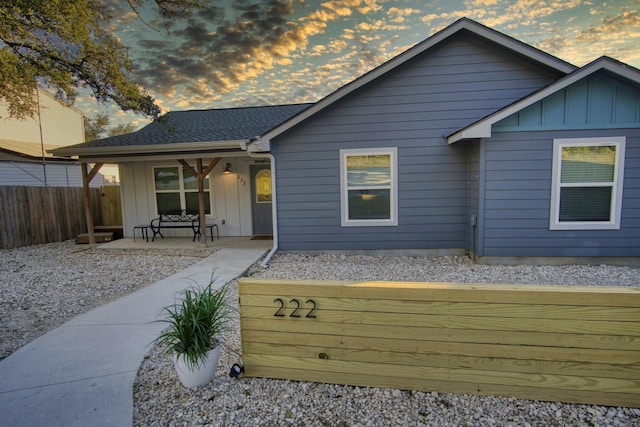 back of property at dusk with fence, covered porch, board and batten siding, and roof with shingles