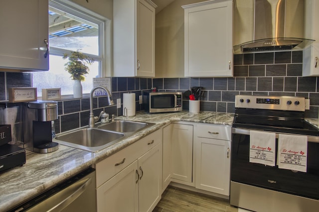 kitchen with decorative backsplash, stainless steel appliances, wall chimney range hood, and a sink