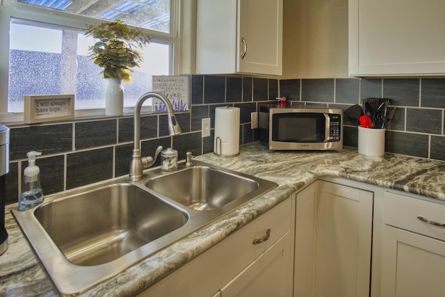 kitchen with tasteful backsplash, stainless steel microwave, white cabinetry, and a sink