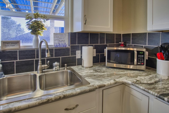 kitchen featuring tasteful backsplash, stainless steel microwave, white cabinetry, and a sink