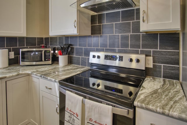 kitchen featuring backsplash, light stone countertops, appliances with stainless steel finishes, exhaust hood, and white cabinets