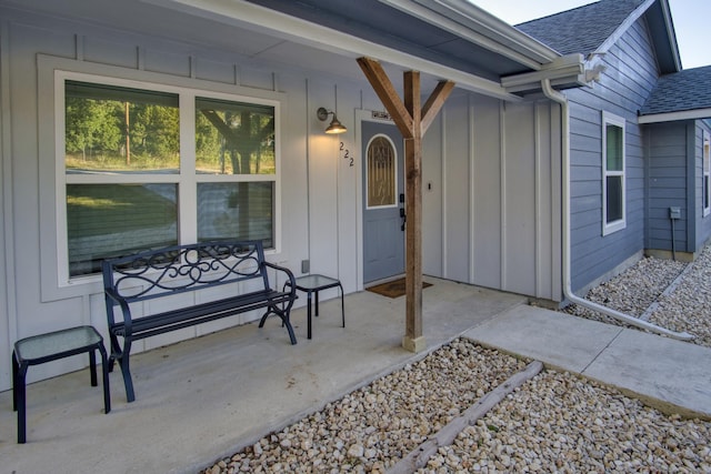 doorway to property with covered porch, board and batten siding, and roof with shingles