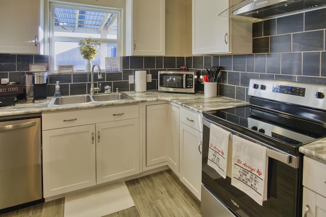 kitchen with a sink, tasteful backsplash, white cabinetry, appliances with stainless steel finishes, and exhaust hood