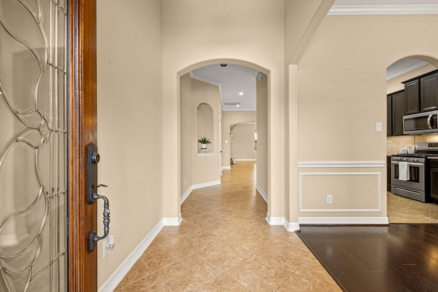 foyer entrance with arched walkways, light tile patterned floors, crown molding, and baseboards