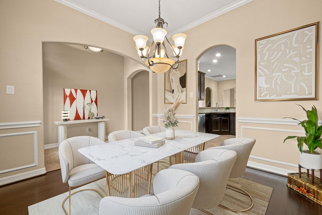 dining room with wood finished floors, arched walkways, ornamental molding, a decorative wall, and a notable chandelier