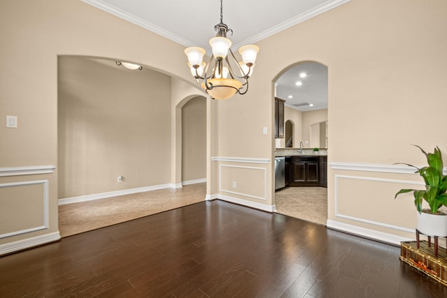 unfurnished dining area with wood finished floors, arched walkways, ornamental molding, a decorative wall, and a chandelier