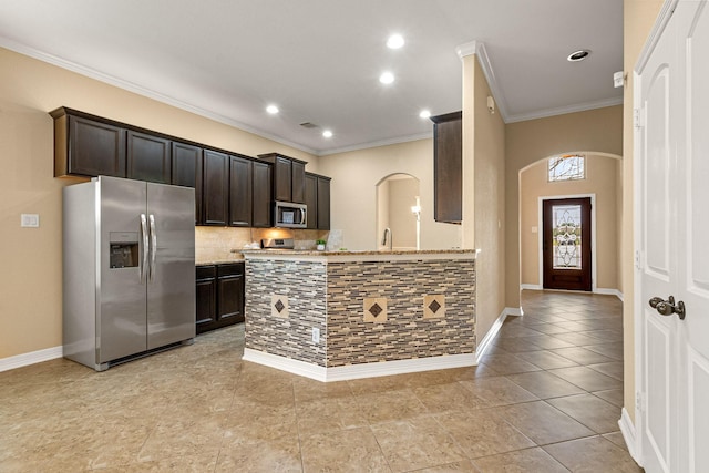 kitchen featuring arched walkways, dark brown cabinetry, appliances with stainless steel finishes, crown molding, and decorative backsplash