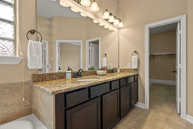 bathroom featuring a spacious closet, double vanity, baseboards, and a sink