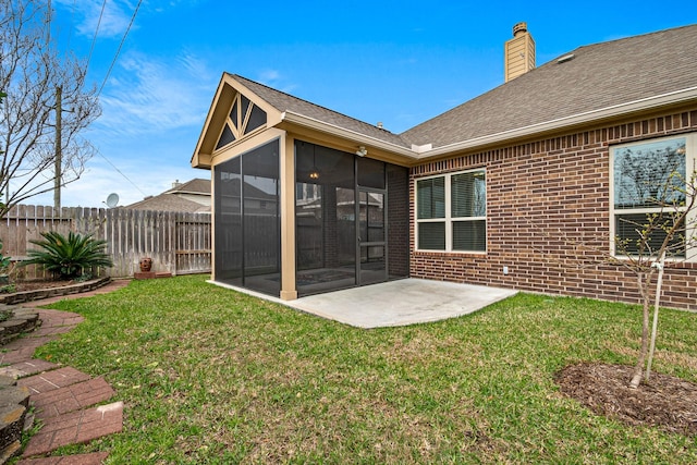 rear view of property featuring fence, a yard, a sunroom, brick siding, and a chimney