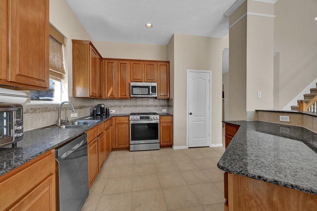 kitchen featuring decorative backsplash, dark stone countertops, light tile patterned flooring, stainless steel appliances, and a sink