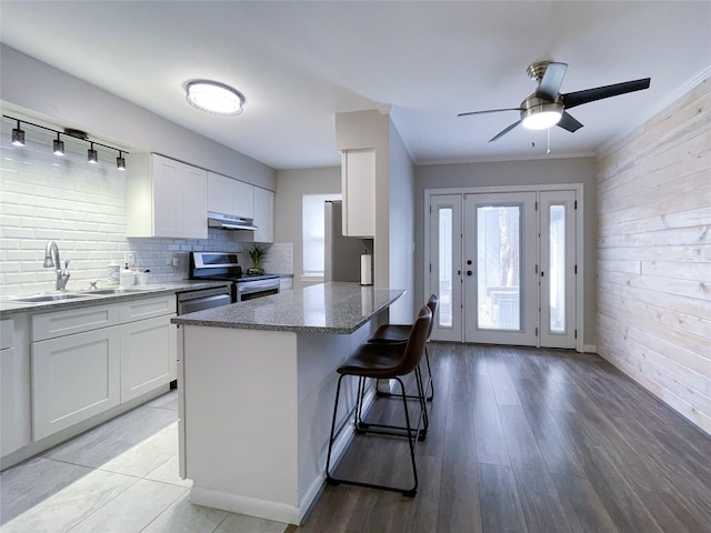 kitchen featuring a breakfast bar, a sink, stainless steel appliances, under cabinet range hood, and white cabinetry