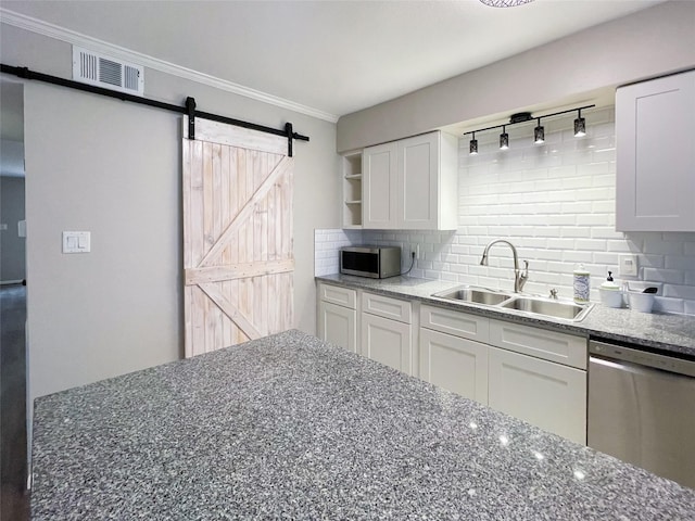 kitchen with a sink, backsplash, white cabinetry, stainless steel appliances, and a barn door