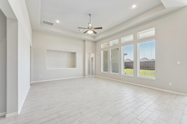 unfurnished living room with a tray ceiling, visible vents, baseboards, and a ceiling fan