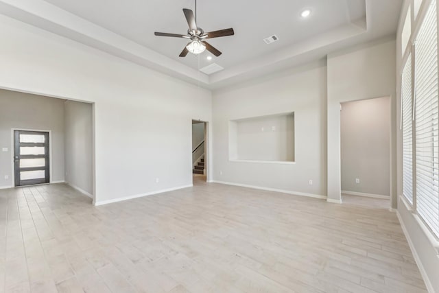 spare room featuring a raised ceiling, a high ceiling, and light wood-style flooring