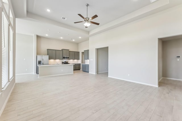 unfurnished living room with visible vents, light wood-style flooring, a raised ceiling, and ceiling fan