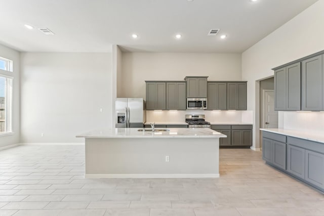 kitchen with stainless steel appliances, visible vents, a kitchen island with sink, and light countertops