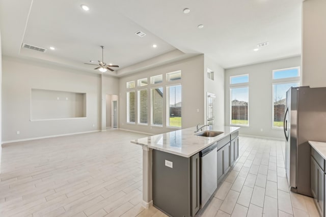 kitchen featuring visible vents, a center island with sink, a tray ceiling, a sink, and appliances with stainless steel finishes