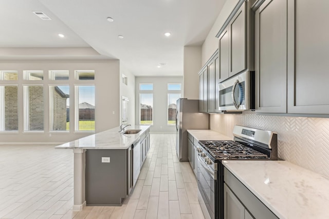 kitchen featuring light stone counters, backsplash, gray cabinetry, and stainless steel appliances