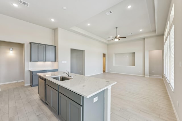 kitchen featuring a center island with sink, dishwasher, a raised ceiling, and a sink