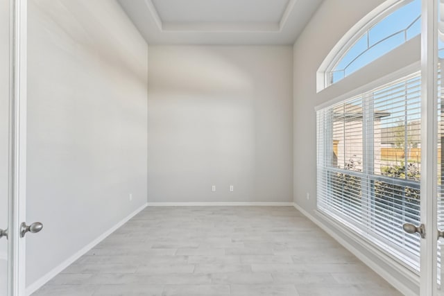 unfurnished room featuring light wood-style flooring, baseboards, and a tray ceiling