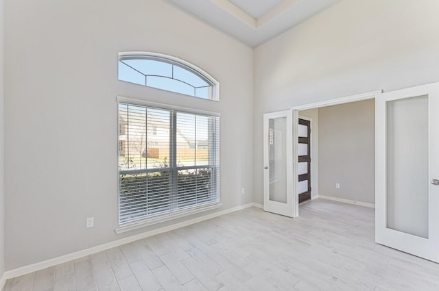 spare room featuring light wood-type flooring, french doors, and baseboards