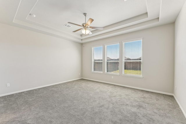 carpeted empty room with baseboards, a raised ceiling, visible vents, and a ceiling fan