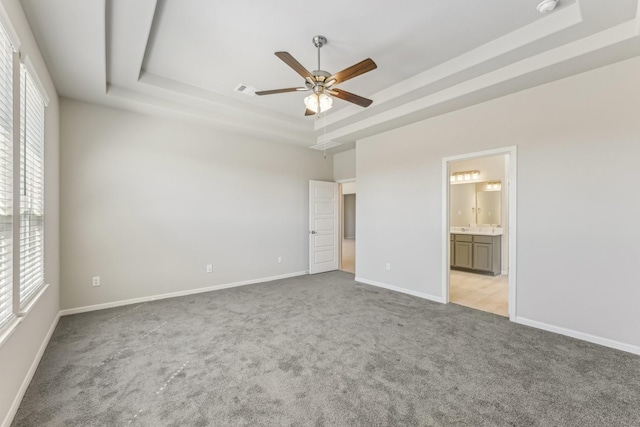 unfurnished bedroom featuring visible vents, connected bathroom, baseboards, a tray ceiling, and light carpet