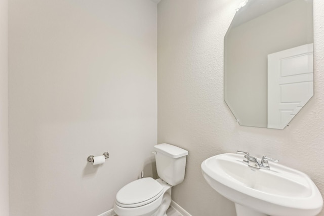 half bath featuring a sink, baseboards, and toilet