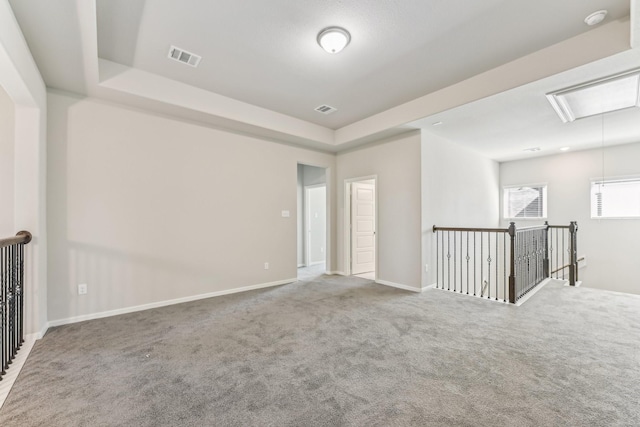 empty room with visible vents, baseboards, attic access, a tray ceiling, and carpet floors