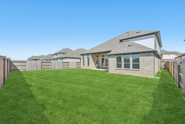 back of house with brick siding, a fenced backyard, a lawn, and roof with shingles