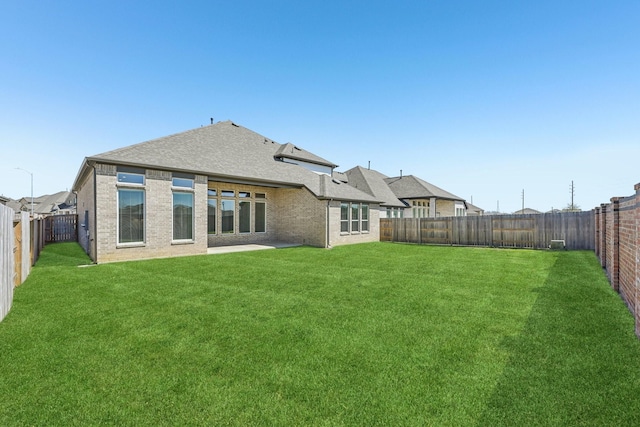 rear view of property with a yard, brick siding, a fenced backyard, and a shingled roof