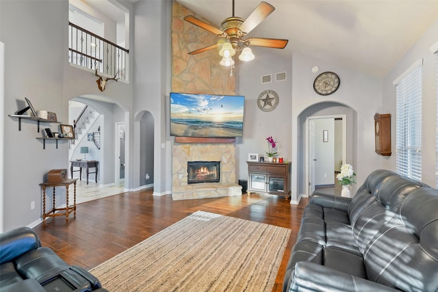 living area with stairway, wood finished floors, baseboards, high vaulted ceiling, and a fireplace