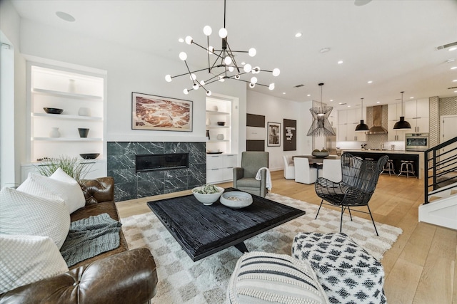 living room featuring built in features, a premium fireplace, stairs, and light wood finished floors