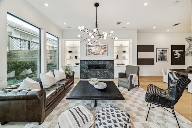 living room featuring light wood finished floors, visible vents, built in shelves, a premium fireplace, and recessed lighting