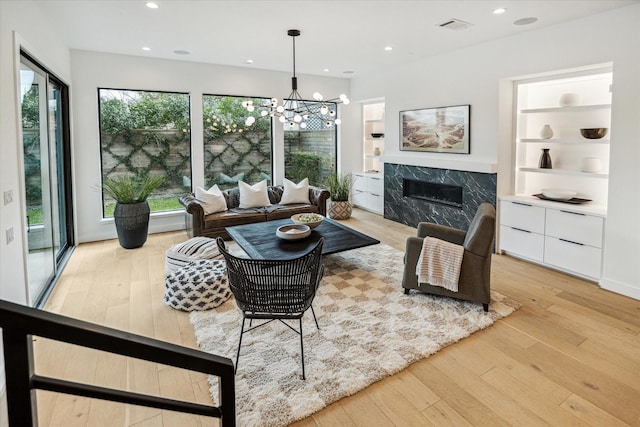 living area with built in features, light wood-style floors, recessed lighting, and a high end fireplace